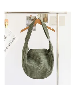 Detalle de un bolso de lona con cuadros verdes colgado de una percha de madera.