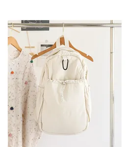 Mochila minimalista de nailon crema presentada en una percha de madera en un ambiente acogedor.