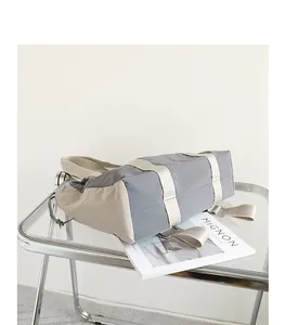 Vista lateral detallada de un bolso tote de nailon gris y beige con cordón ajustable