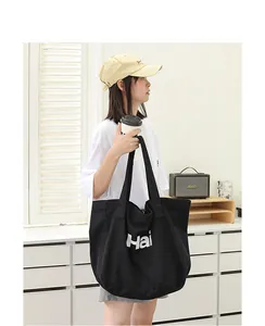 Detailed lifestyle view of a large black canvas tote bag with white letter print.