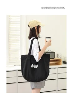 Detail view of a black canvas tote bag with white letter print on a woman's shoulder