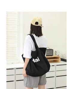 Back view of a model carrying a large black canvas tote bag with letter print