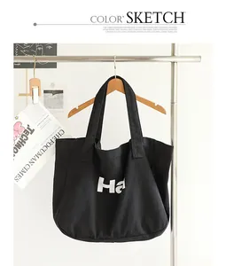 Detailed view of washed black canvas tote bag with white letter print on a hanger