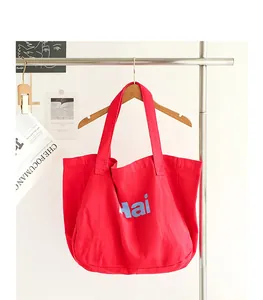 Detailed shot of a red canvas tote bag with blue 'Hai' letter print hanging on a hanger