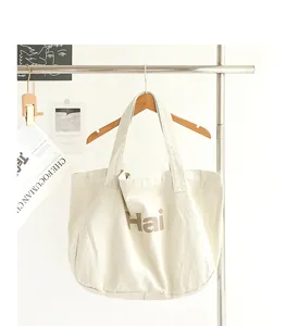Close-up detail of cream canvas tote bag with 'Hai' print hanging on wooden hanger