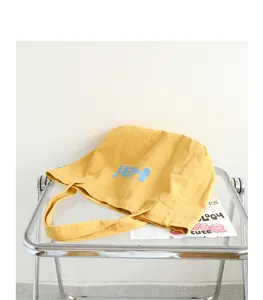 Close-up view of a yellow washed canvas tote bag with Hai print on a modern transparent chair