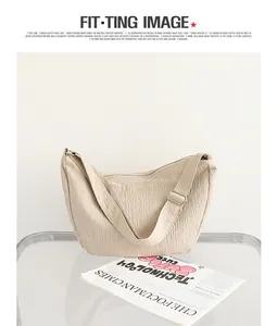 Detail of beige wrinkled nylon shoulder bag with adjustable strap on glass table.