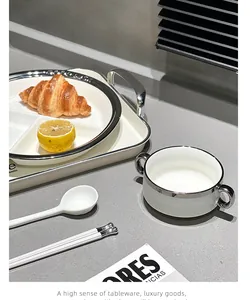 Detailansicht eines weißen Keramik-Frühstücksteller-Sets mit Silberrand auf Steintisch