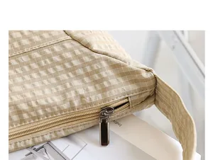 Primer plano detallado de la cremallera metálica de este bolso de lona a cuadros beige