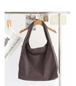 Gran bolso tote de lona a cuadros colgado de una percha de madera en un entorno luminoso.
