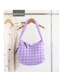 Detail of a purple quilted nylon shoulder bag hanging on a wooden clothes rack with a sweater