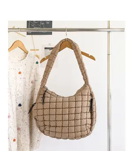 Detailed view of a khaki quilted puffy nylon shoulder bag hanging on a minimalist wooden hanger