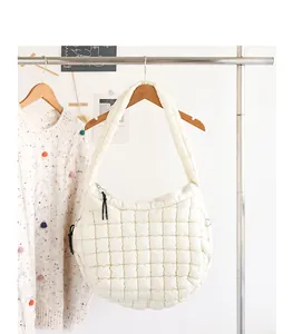 Detailed view of white quilted nylon shoulder bag hanging on a wooden rack in a minimalist room