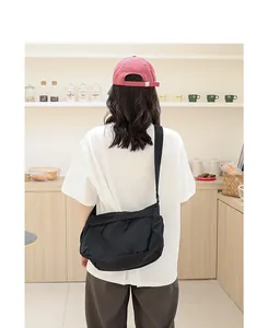 Rückansicht einer Frau mit einer schwarzen minimalistischen Nylon-Umhängetasche im Café