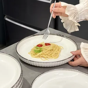 Assiette ronde en céramique blanche avec bord argenté et texture nervurée pour pâtes.