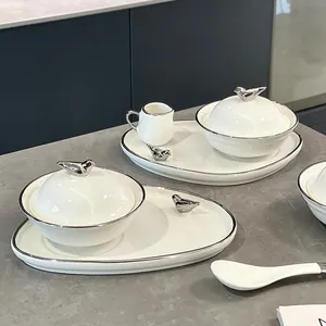 Moderne witte keramische soep- en dessertkommen met zilveren vogeldeksels en dienbladen