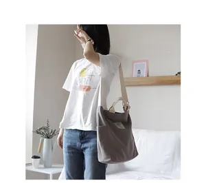 Detail view of a minimalist gray canvas shoulder bag worn by a model in a casual setting.
