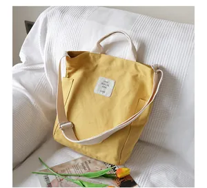 Detailed view of a yellow canvas shoulder bag on a white textured background