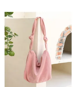 A stylish pink corduroy hobo bag featuring unique knot strap details hanging against a white wall.