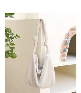 Detail of cream corduroy crossbody bag with decorative knotted straps hanging on wall