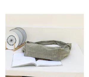 Lifestyle detail showing a green corduroy crossbody bag with unique knotted strap design.