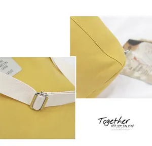Close-up detail of yellow canvas bag stitching and white strap with metal buckle.