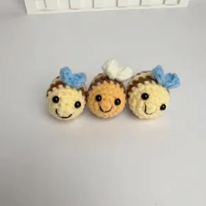 Close-up of three adorable handmade crochet bee keychains in soft yellow and orange yarn colors