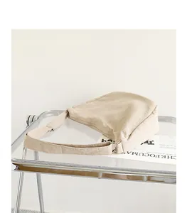 Close-up of a beige pleated nylon shoulder bag on a minimalist transparent table.