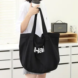 Casual black canvas tote bag with letter print carried by a person in a minimalist room