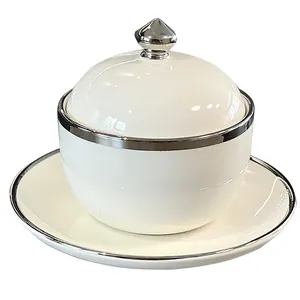 Elegante olla de cerámica blanca con tapa y platillo, con ribete plateado pulido.
