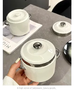 Detailed view of a white ceramic stew pot with elegant silver handles and lid.