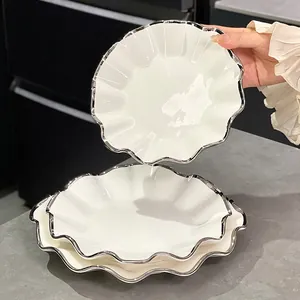 Assiettes en céramique blanche élégantes avec bords festonnés argentés dans une cuisine