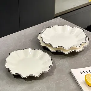 Assiettes élégantes en céramique blanche avec bordure argentée ondulée sur fond gris
