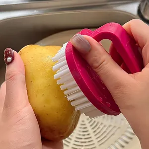 Action shot showing a pink egg-shaped multi-purpose brush cleaning a fresh potato