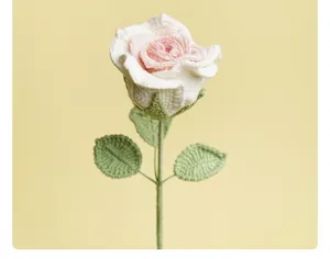 Detailed macro view of a handmade white and pink crocheted rose with green leaves