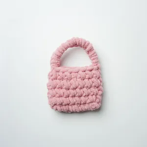 Primer plano de un mini bolso rosa tejido a mano con hilo de chenilla suave y esponjoso