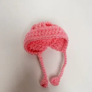 Detailed macro shot of a mini pink crochet doll hat featuring tie strings and pom-pom ends