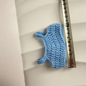 Detailed view of a blue handmade crochet doll sweater being measured with a metal tape