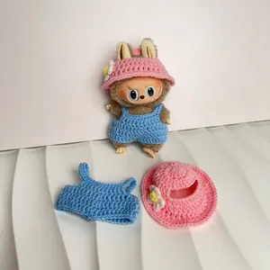 Crochet doll clothes set with pink hat and blue overalls displayed on a plush doll