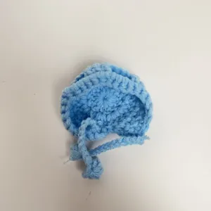 Close-up of light blue mini crochet doll hat with hand-knitted texture and ties
