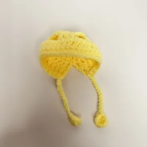Close-up of a handmade yellow crocheted mini hat with braided ties for doll accessories