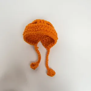 Close-up of a handmade orange crochet mini hat for dolls with side ties and pom-poms