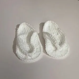 Nahaufnahme der weichen handgehäkelten Textur der weißen Baby-Flip-Flop-Hausschuhe.