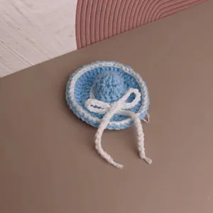 Detail view of a handmade blue mini crocheted sun hat with white bow for dolls