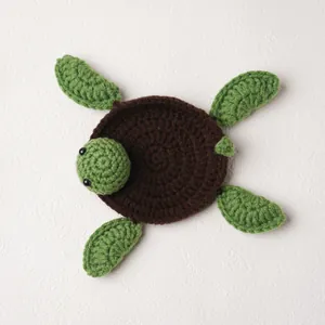 Handmade knitted crochet turtle coaster with brown shell and green fins for desk protection