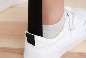 Close-up detail shot of a black shoehorn assisting a foot into a white casual sneaker