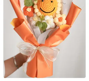 Detail van handgemaakt gehaakt zonnebloemboeket met oranje papier en een witte strik.
