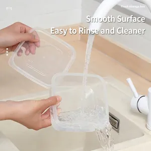 Transparent plastic food storage container being rinsed under a running water faucet