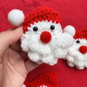 Detailed close-up of a handmade crochet Santa Claus brooch with red hat and white beard.