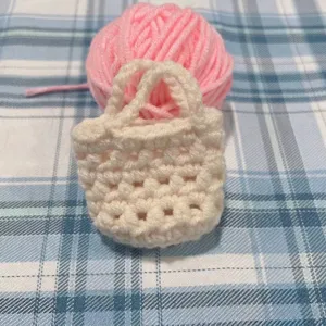Nahaufnahme eines handgefertigten cremefarbenen Häkel-Mini-Taschenanhängers